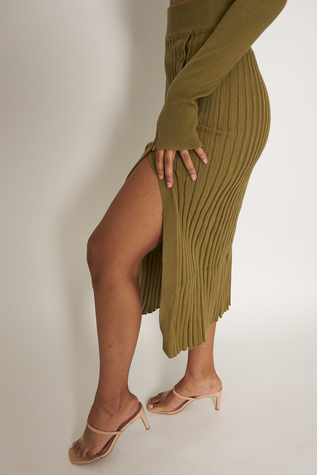 Show Me Leg is an olive green sultry pleated, mid-thigh slit sweater skirt paired with a long sleeve crop top. The crop top has a thumb hole feature that allows for easy layering and provides a sleek look. The skirt has a natural hourglass shape that helps accentuate your hips, slims your waist creating the hourglass effect when put on. 